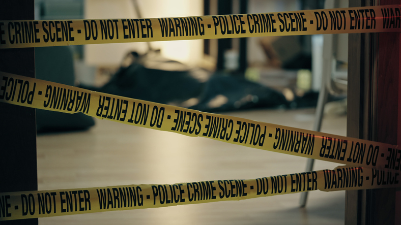 The body of a dead person lying on the floor covered with plastic corpse bag, murder scene secured by warning police tape Woman Found Dead in Delhi Hotel, Man Hospitalised After Apparent Suicide Attempt